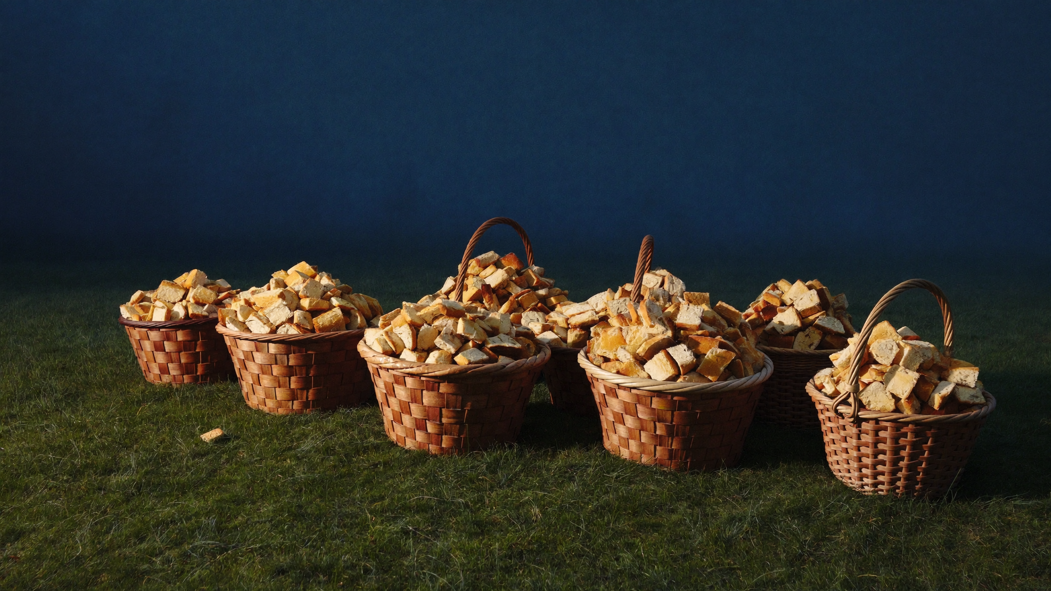 Twelve woven baskets brimming with bread fragments on trampled grass in golden evening light